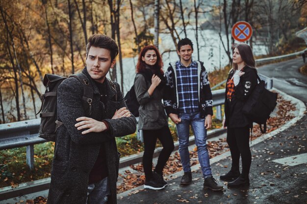 Un grupo de jóvenes turistas tiene un agradable paseo por el bosque de otoño en la carretera lateral.