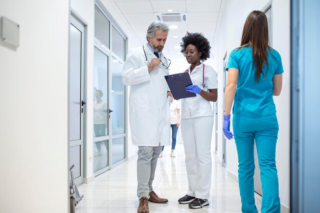 Grupo de médicos con portapapeles discutiendo a lo largo del pasillo del hospital Doctor y enfermera informando informe médico