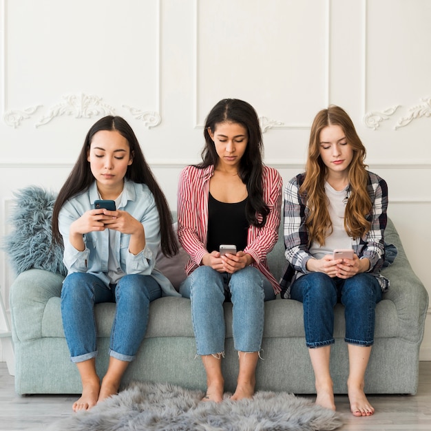 Grupo multiétnico de adolescentes sentados usando teléfonos