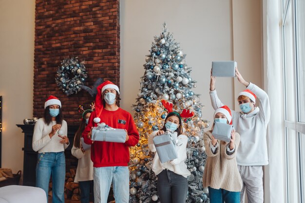 Grupo multiétnico de amigos con gorro de Papá Noel sonriendo y posando con regalos en las manos