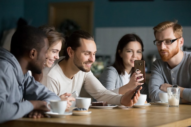 Grupo multiétnico de amigos hablando y usando teléfonos inteligentes en la reunión