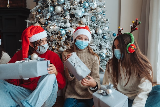 Grupo multiétnico de amigos con sombreros de Santa sonriendo y posando para la cámara con regalos en las manos. El concepto de celebrar año nuevo y Navidad bajo restricciones de coronavirus. vacaciones en cuarentena