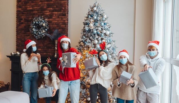 Grupo multiétnico de amigos con sombreros de Santa sonriendo y posando con regalos en las manos. El concepto de celebrar la Navidad bajo las restricciones del coronavirus.