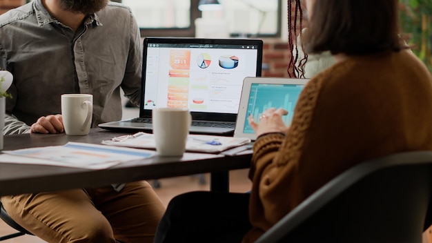 Grupo multiétnico de colegas que trabajan en análisis de gráficos con tableta digital, utilizando información de investigación en línea para crear informes infográficos. Personas analizando diagramas en la sala de juntas.