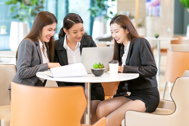 Grupo de negocios asiáticos femeninos uniformes de negocios reunión informal en línea con el cliente en una computadora portátil con antecedentes de oficina de diseño moderno