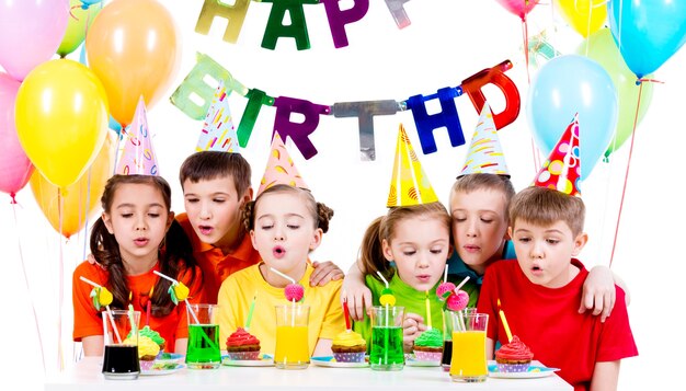Grupo de niños en camisetas de colores que soplan velas en la fiesta de cumpleaños - aislado en un blanco.