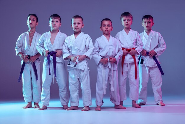 Grupo de niños entrenando karate de artes marciales aislado sobre fondo de estudio púrpura en neón