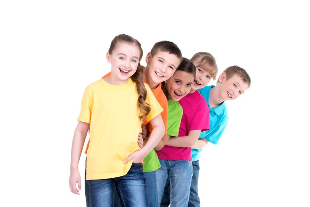 Grupo de niños felices en camisetas de colores están uno detrás del otro sobre fondo blanco.