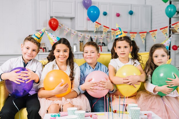 Grupo de niños felices con globo sentado en el sofá