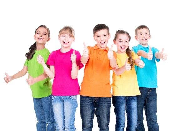 Grupo de niños felices con el pulgar hacia arriba firmar en coloridas camisetas de pie juntos, aislados en blanco.
