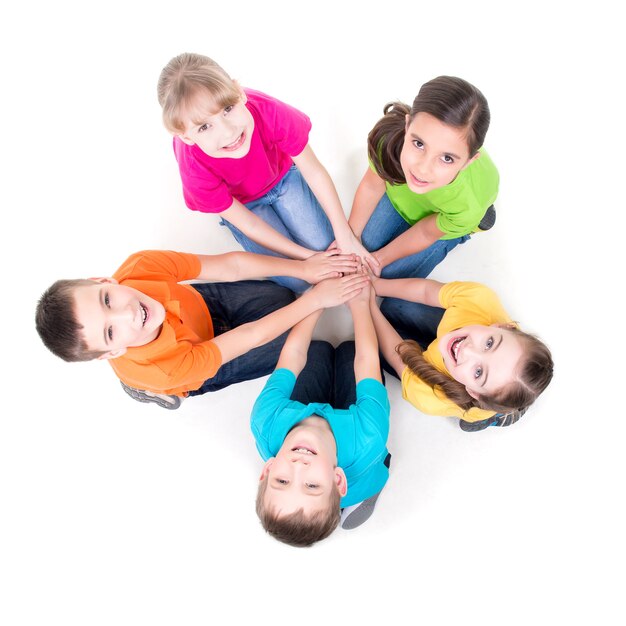 Grupo de niños felices sentados en el suelo en un círculo tomados de la mano y mirando hacia arriba - aislado en blanco.