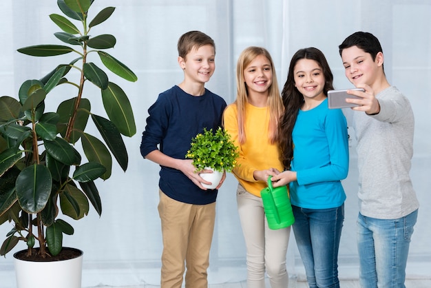 Foto gratuita grupo de niños regando flores y tomando selfie