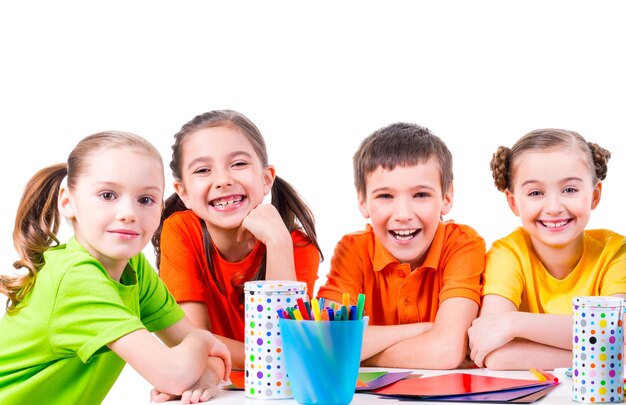 Grupo de niños sentados en una mesa con marcadores, crayones y cartulina de colores