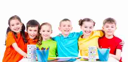 Foto gratuita grupo de niños sentados en una mesa con marcadores, crayones y cartulina de colores