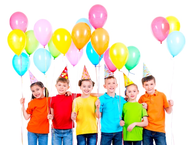 Grupo de niños sonrientes en camisetas de colores y gorros de fiesta con globos sobre un fondo blanco.