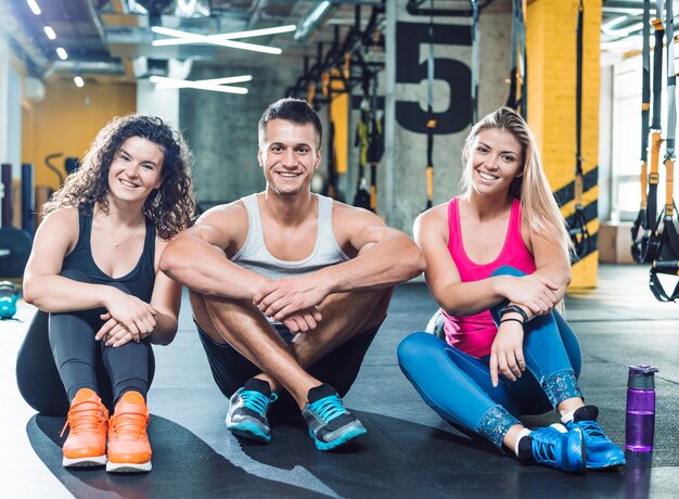 Grupo de personas atléticas felices que se sientan en piso en gimnasio