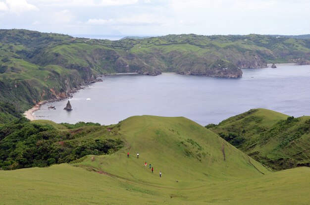 Grupo de personas caminando por las montañas alrededor de un mar rodeado de vegetación bajo un cielo azul