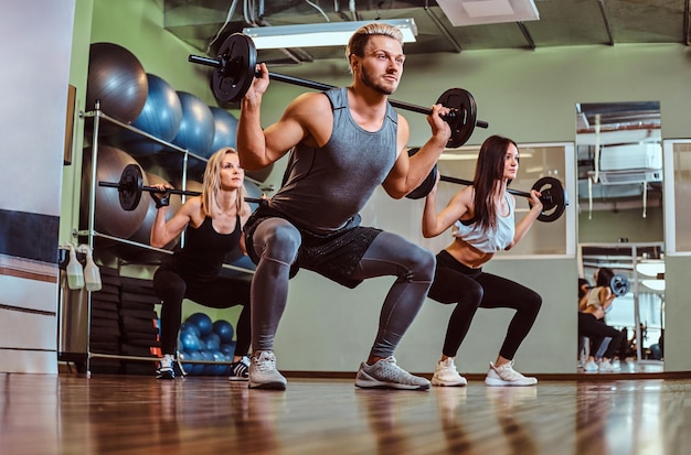 Grupo de personas haciendo ejercicio con barra haciendo sentadillas en el gimnasio.