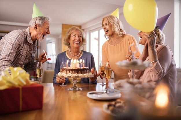Grupo de personas mayores alegres cantando mientras celebran el cumpleaños de la mujer en casa