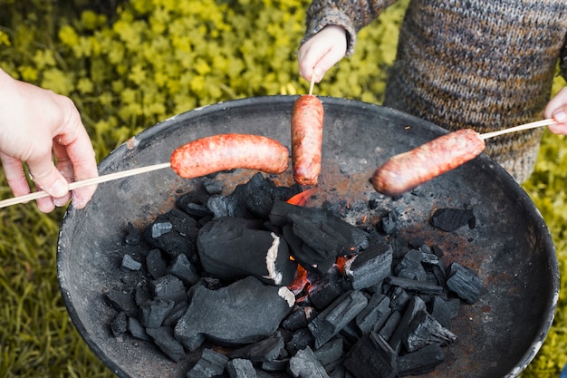 Grupo de personas preparando salchichas en barbacoa portátil