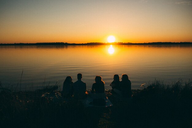 Grupo de personas sentadas junto al mar disfrutando de la hermosa vista del atardecer