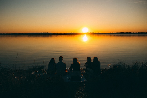 Grupo de personas sentadas junto al mar disfrutando de la hermosa vista del atardecer