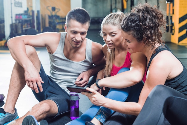 Grupo de personas sentadas en el piso mirando teléfono inteligente en el gimnasio