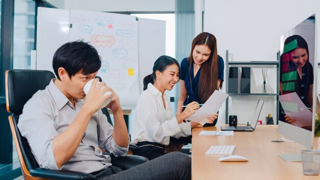 Grupo de proceso colaborativo de empresarios multiculturales en ropa casual elegante que se comunican y usan tecnología mientras trabajan juntos en una oficina creativa. El equipo asiático de jóvenes profesionales trabaja.