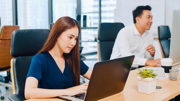 Grupo de proceso colaborativo de empresarios multiculturales en ropa casual elegante que se comunican y usan tecnología mientras trabajan juntos en una oficina creativa. El equipo asiático de jóvenes profesionales trabaja.