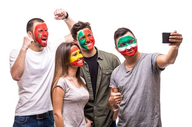 Grupo de simpatizantes de personas, fanáticos de equipos nacionales pintados con la cara de la bandera de Portugal, España, Marruecos, Irán toman selfie desde el teléfono. Fans de las emociones.