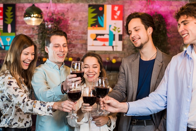 Grupo de sonrientes amigas y amigos brindando vino en un club