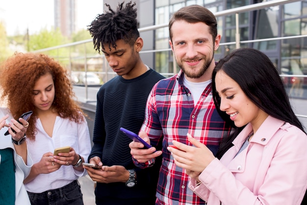 Grupo de sonrientes amigos multirraciales usando teléfonos inteligentes