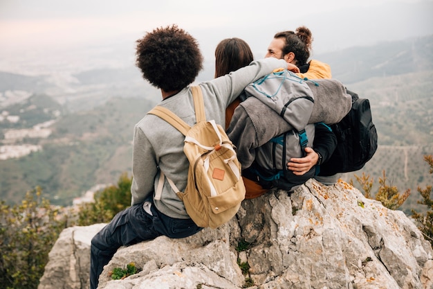 Grupo de tres amigos sentados en la cima del pico de la montaña mirando la vista
