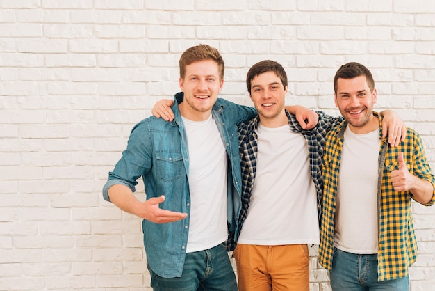 Foto gratuita grupo de tres amigos varones de pie juntos contra la pared blanca