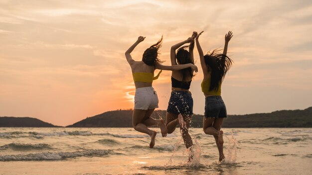 Grupo de tres mujeres jóvenes asiáticas saltando en la playa