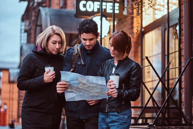 Grupo de turistas que buscan un lugar en el mapa cerca de un café afuera.