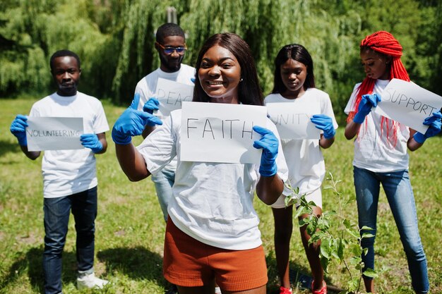 Grupo de voluntarios africanos felices sostienen un tablero en blanco con un signo de fe en el parque África voluntariado personas caritativas y concepto de ecología