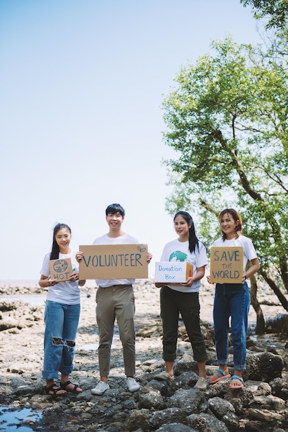 Grupo de voluntarios sostienen un cartel de voluntario en el evento del día mundial del medio ambiente conservación voluntaria recogen basura de plástico y espuma en el área del bosque de manglaresVoluntariado para salvar el concepto mundial