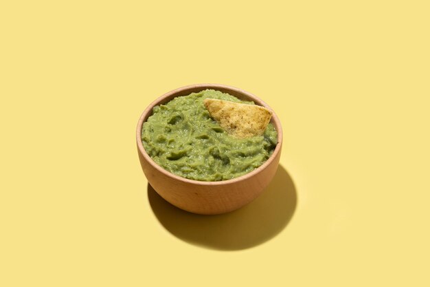 Guacamole mexicano con nacho chip en tazón de madera sobre fondo amarillo