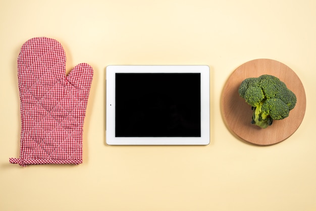 Foto gratuita guante de horno mitt; tableta digital y brócoli en bandeja de madera sobre fondo beige.