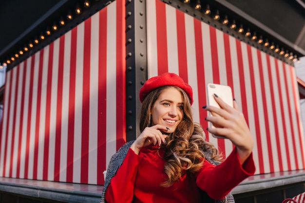 Guapa chica morena con expresión de cara feliz haciendo selfie sobre fondo rayado