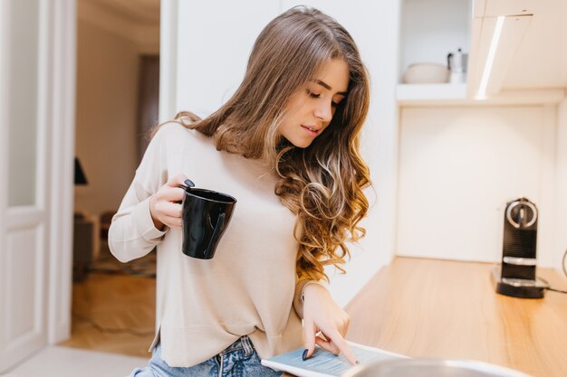 Guapa mujer europea con peinado rizado leyendo una revista en su habitación