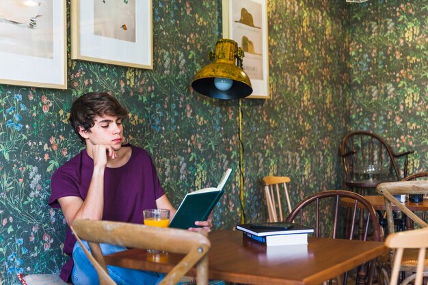 Guapo adolescente leyendo en café