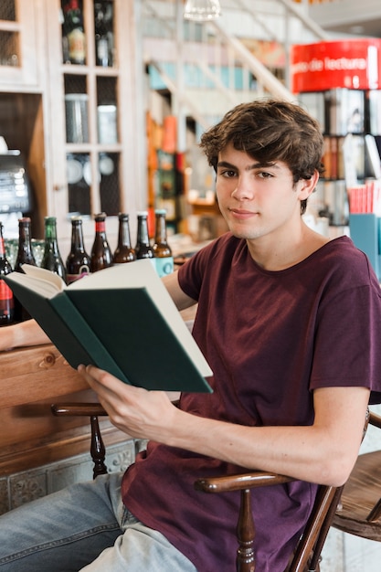 Guapo adolescente masculino con libro mirando a la cámara