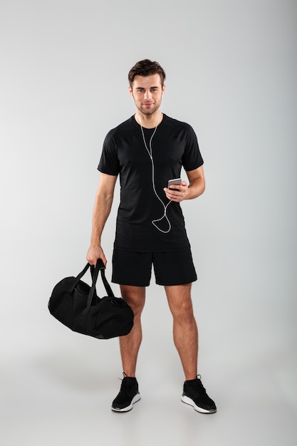 Guapo alegre joven deportista con teléfono escuchando música