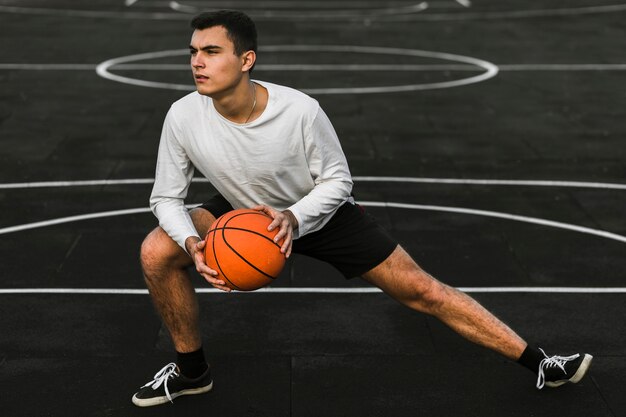 Guapo atleta estirando en cancha de baloncesto