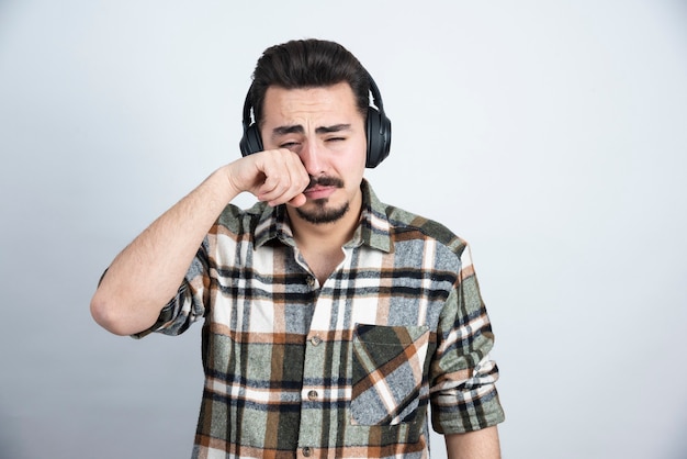 Foto gratuita guapo en auriculares llorando en la pared blanca.