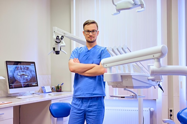 Guapo dentista masculino en una habitación con equipo médico en segundo plano.