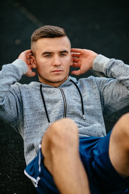 Guapo deportista haciendo prensa, empuja hacia arriba, vistiendo ropa deportiva al aire libre