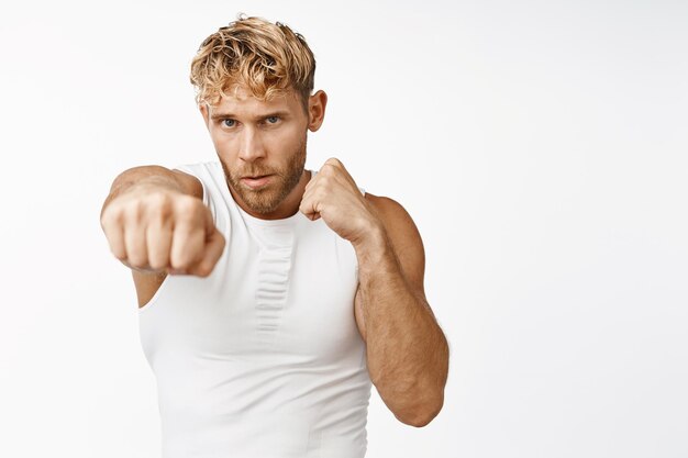 Guapo deportista practica movimientos de lucha extiende el puño y golpea el boxeo de sombra en el gimnasio de pie sobre fondo blanco